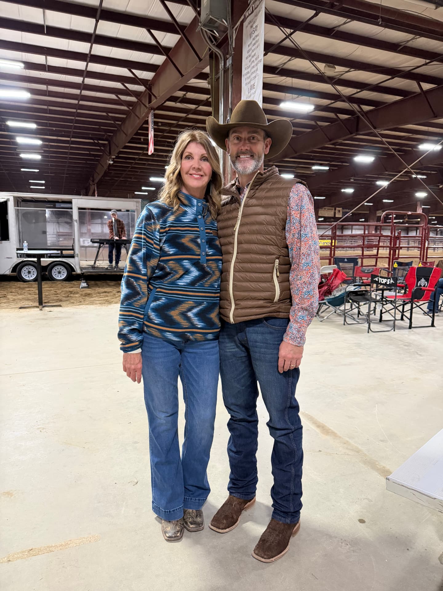 A couple standing together in an arena, the man wearing a cowboy hat
