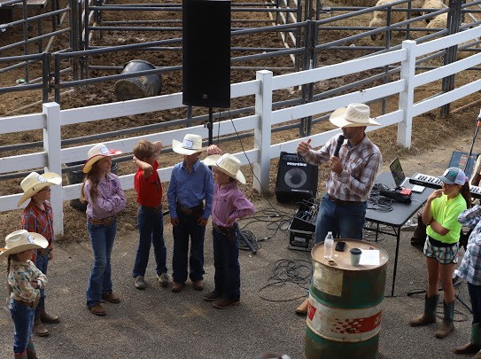 Children in cowboy hats standing with a speaker at a gathering
