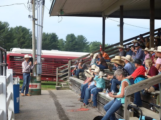 Families in cowboy hats seated on bleachers listening to a speaker