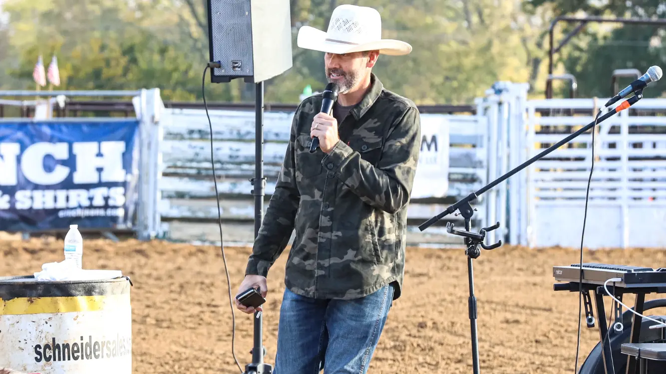 Pastor in a white cowboy hat speaking into a microphone in an outdoor arena